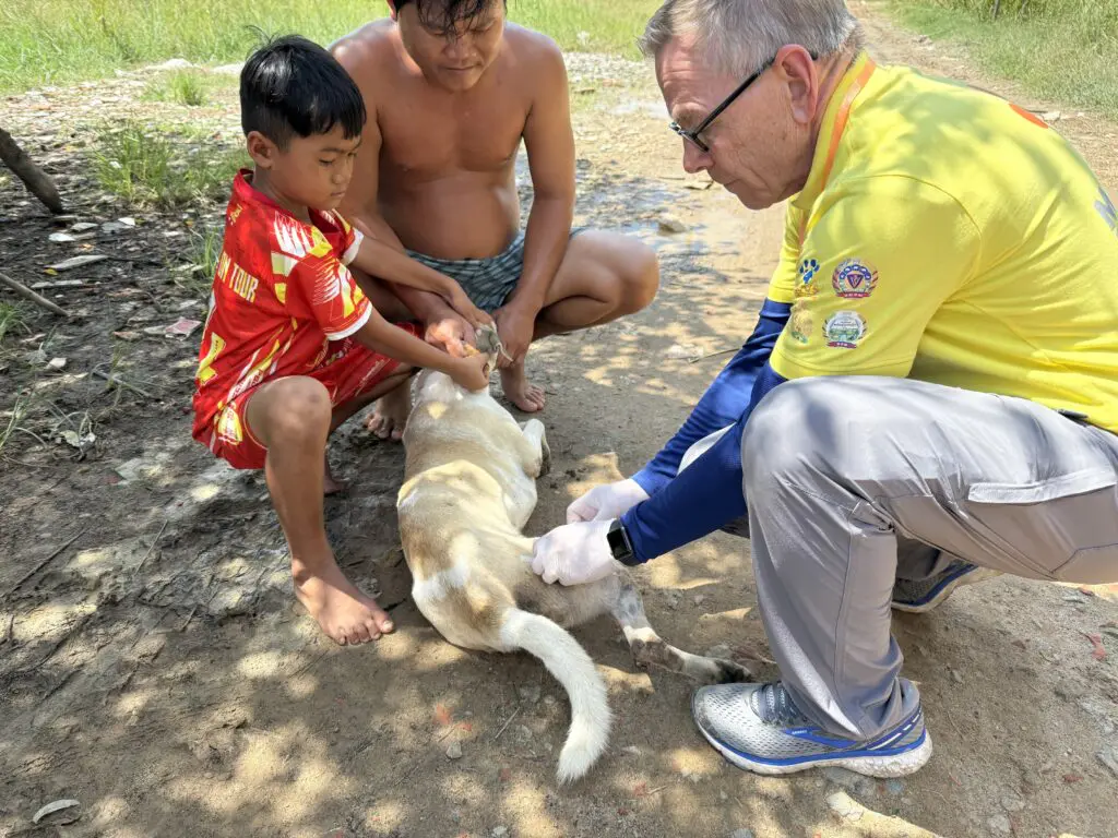 Dr. Link Welborn vaccinating a dog with two children from Phnom Penh