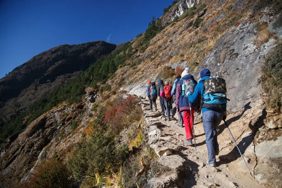 Travellers follow a narrow path on a mountainside. Bright sunny day